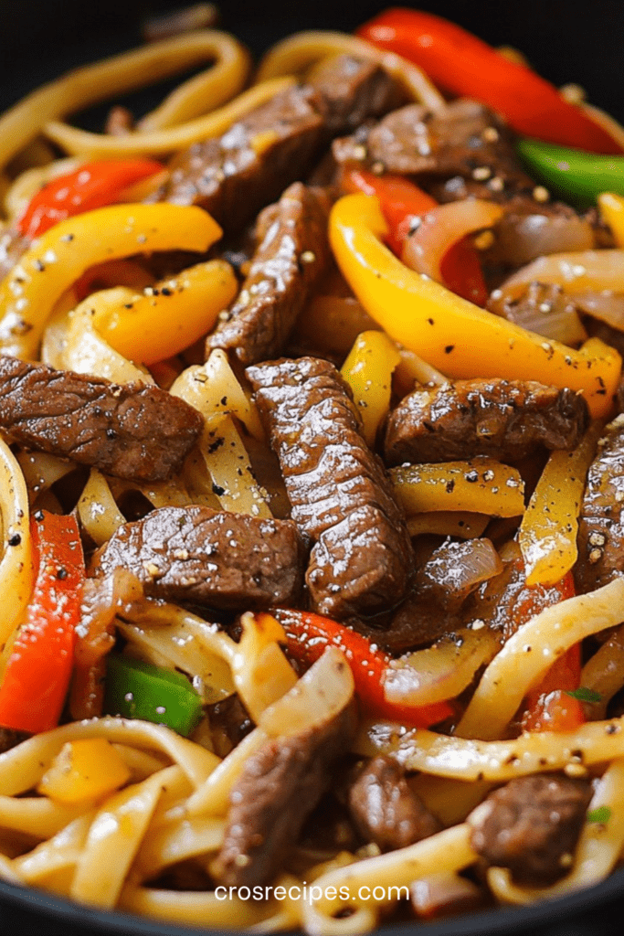 Assiette de pâtes avec lamelles de steak grillées et poivrons colorés, légèrement caramélisés, garnie de persil frais dans une poêle chaude.