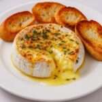 Camembert entier fondu au four avec thym et miel, servi dans sa boîte en bois avec morceaux de pain grillé pour tremper