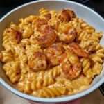 Assiette de pâtes crémeuses aux crevettes et au poulet, nappées d’une sauce épicée onctueuse, servies bien chaudes avec fromage fondu et assaisonnement doré.