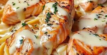 Assiette de pâtes crémeuses au saumon grillé nappées d’une sauce fromagère onctueuse, garnies de persil frais et servies bien chaudes.