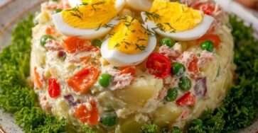 Salade russe crémeuse avec pommes de terre en dés, thon émietté, œufs en quartiers, petits pois et carottes, décorée d’herbes fraîches.