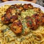 Assiette de spaghetti crémeux au poulet doré, nappés d’une sauce onctueuse à l’ail et au parmesan, décorés de persil frais dans un cadre chaleureux.