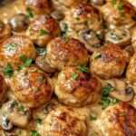 Boulettes de poulet dorées servies dans une sauce crémeuse aux champignons avec persil frais, accompagnées de pâtes ou de riz.