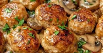 Boulettes de poulet dorées servies dans une sauce crémeuse aux champignons avec persil frais, accompagnées de pâtes ou de riz.