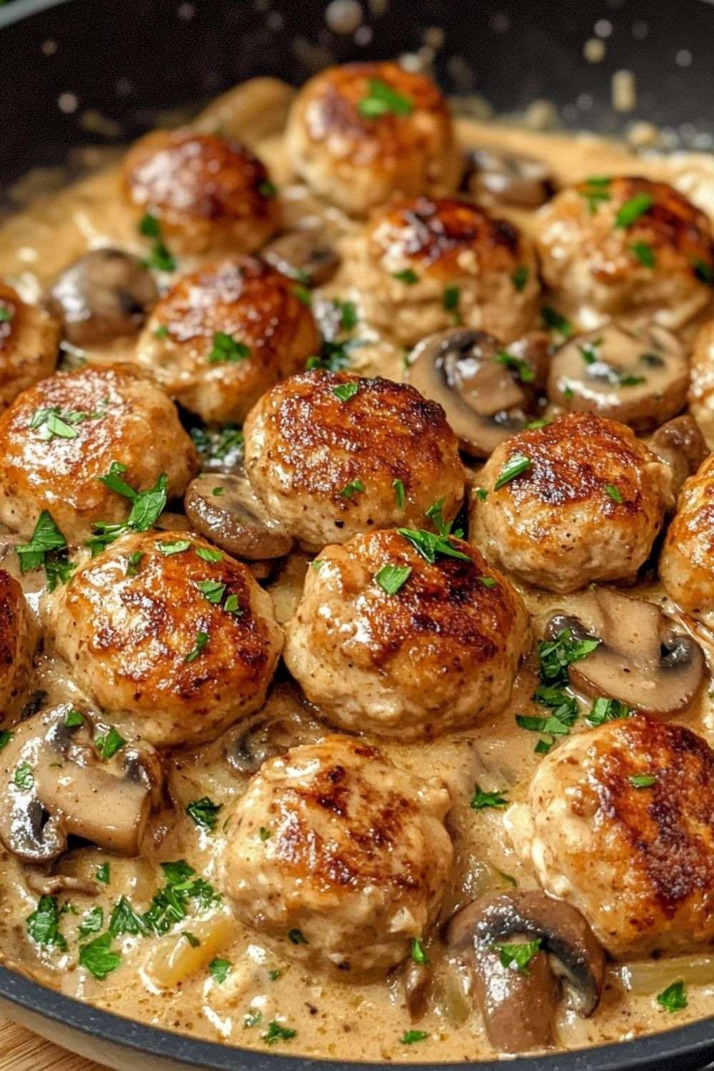 Boulettes de poulet dorées servies dans une sauce crémeuse aux champignons avec persil frais, accompagnées de pâtes ou de riz.