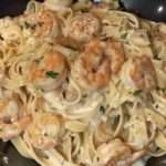 Assiette de pâtes crémeuses aux crevettes dorées, sauce onctueuse à l’ail et parmesan, garnie de persil frais.