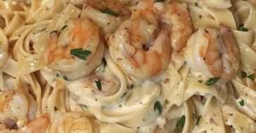 Assiette de pâtes crémeuses aux crevettes dorées, sauce onctueuse à l’ail et parmesan, garnie de persil frais.