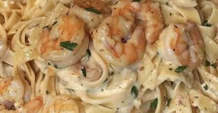 Assiette de pâtes crémeuses aux crevettes dorées, sauce onctueuse à l’ail et parmesan, garnie de persil frais.