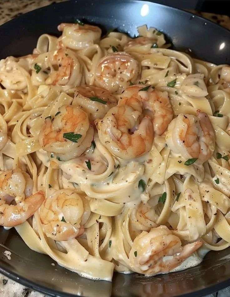 Assiette de pâtes crémeuses aux crevettes dorées, sauce onctueuse à l’ail et parmesan, garnie de persil frais.