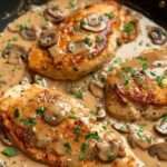Blancs de poulet dorés nappés d’une sauce crémeuse aux champignons et oignons, garnis de persil frais dans une poêle.
