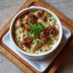 Œufs cocotte au poulet gratiné et crème servis dans des ramequins, avec fromage doré, crème onctueuse, morceaux de poulet fondants et persil frais.