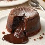 Fondant au chocolat individuel, légèrement craquelé à l’extérieur, avec un cœur coulant intense au chocolat noir, servi chaud sur une assiette avec une texture brillante.