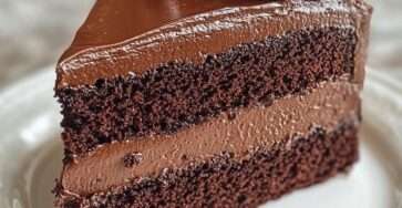 Gâteau au chocolat coupé en deux couches, garni d’une mousse aérienne, recouvert d’une ganache brillante et lisse, avec une texture fondante et intense.