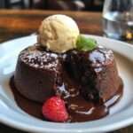 Fondants au chocolat noir avec cœur coulant, servis tièdes dans de petites assiettes avec une boule de glace vanille et quelques fruits rouges.