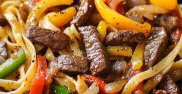 Assiette de pâtes avec lamelles de steak grillées et poivrons colorés, légèrement caramélisés, garnie de persil frais dans une poêle chaude.