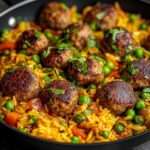 Assiette de riz coloré aux petits pois et poivrons, surmonté de boulettes de viande dorées, garni d’herbes fraîches, présentation chaleureuse.