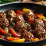 Assiette de boulettes de viande maison mijotées dans une sauce tomate aux poivrons rouges et jaunes, servies chaudes avec persil frais.