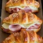 Croissants jambon-fromage gratinés sortant du four, dorés et croustillants, garnis de fromage fondant et saupoudrés de graines de sésame