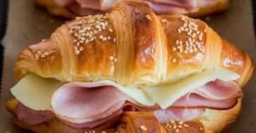 Croissants jambon-fromage gratinés sortant du four, dorés et croustillants, garnis de fromage fondant et saupoudrés de graines de sésame