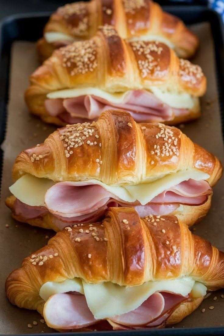 Croissants jambon-fromage gratinés sortant du four, dorés et croustillants, garnis de fromage fondant et saupoudrés de graines de sésame