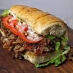 Sandwich Chopped Cheese garni de bœuf haché grillé, fromage fondant, laitue, tomates et sauce dans un pain brioché moelleux.