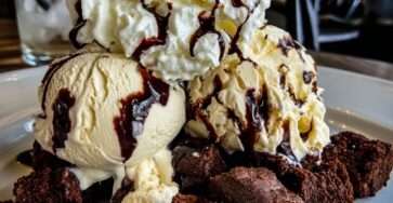 Brownie glacé servi en coupe avec morceaux de brownie fondant, boules de glace vanille, sauce chocolat tiède, chantilly et copeaux de chocolat.