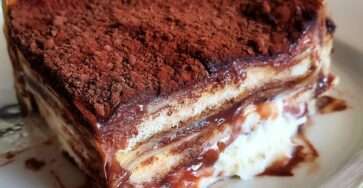Gâteau familial façon tiramisu chocolat servi dans un grand plat, avec couches de biscuits fondants, crème mascarpone, ganache brillante et cacao amer.