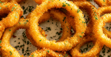 Onion rings croustillants maison servis chauds avec une panure dorée, du persil frais et une sauce crémeuse au ketchup et paprika.