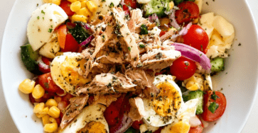 Macédoine revisitée au thon et œufs servie dans un grand plat, avec pommes de terre, tomates cerises, concombre, brocoli, maïs et sauce crémeuse.