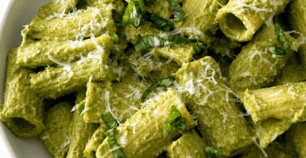 Pâtes crémeuses au pesto vert servies dans une assiette creuse avec parmesan râpé, basilic frais et sauce verte onctueuse.