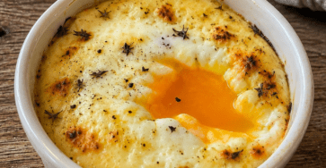 Œufs cocotte crème fromage servis dans des ramequins individuels, avec un jaune coulant, une crème onctueuse, du fromage fondu et quelques herbes fraîches sur le dessus.