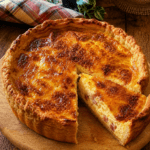 Quiche Lorraine bien dorée servie dans un moule à tarte, avec une pâte brisée croustillante, une garniture moelleuse aux œufs, crème fraîche et lardons, accompagnée d’une salade verte.