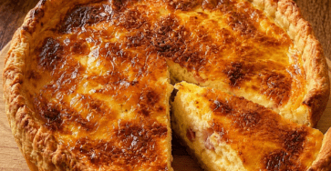 Quiche Lorraine bien dorée servie dans un moule à tarte, avec une pâte brisée croustillante, une garniture moelleuse aux œufs, crème fraîche et lardons, accompagnée d’une salade verte.