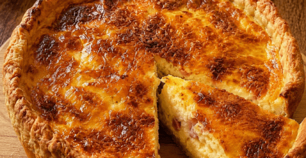 Quiche Lorraine bien dorée servie dans un moule à tarte, avec une pâte brisée croustillante, une garniture moelleuse aux œufs, crème fraîche et lardons, accompagnée d’une salade verte.
