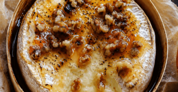 Camembert rôti au miel et noix servi bien chaud dans sa boîte en bois, avec un cœur de fromage coulant, des noix croquantes, du thym et du pain grillé à tremper.