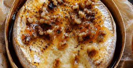 Camembert rôti au miel et noix servi bien chaud dans sa boîte en bois, avec un cœur de fromage coulant, des noix croquantes, du thym et du pain grillé à tremper.