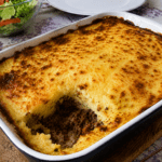 Hachis Parmentier gratiné maison servi dans un plat familial, avec une couche de purée dorée au fromage, une viande hachée fondante dessous et une texture crémeuse visible à la cuillère.