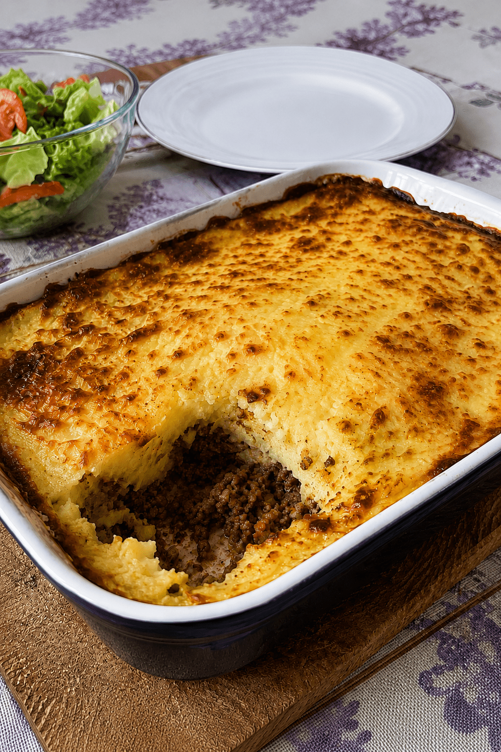 Hachis Parmentier gratiné maison servi dans un plat familial, avec une couche de purée dorée au fromage, une viande hachée fondante dessous et une texture crémeuse visible à la cuillère.
