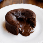 Moelleux au chocolat cœur fondant servi chaud dans une assiette, ouvert à la cuillère avec un cœur de chocolat coulant, une texture moelleuse et une surface légèrement craquelée.