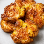 Pommes de terre écrasées croustillantes au parmesan, bien dorées au four, avec une surface croustillante, des herbes et du parmesan gratiné.