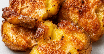 Pommes de terre écrasées croustillantes au parmesan, bien dorées au four, avec une surface croustillante, des herbes et du parmesan gratiné.