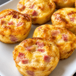 Mini quiches sans pâte au jambon et fromage, dorées dans des moules à muffins, avec une texture moelleuse et une garniture fondante.