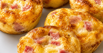 Mini quiches sans pâte au jambon et fromage, dorées dans des moules à muffins, avec une texture moelleuse et une garniture fondante.
