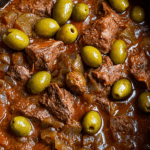 Bœuf mijoté aux olives vertes servi dans une cocotte, avec morceaux de viande fondants, sauce tomate épaisse, oignons et olives vertes.