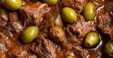 Bœuf mijoté aux olives vertes servi dans une cocotte, avec morceaux de viande fondants, sauce tomate épaisse, oignons et olives vertes.
