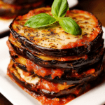 Millefeuille italien d’aubergines gratinées servi dans un plat, avec couches d’aubergines dorées, sauce tomate, mozzarella fondue, parmesan et basilic frais.