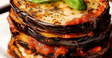 Millefeuille italien d’aubergines gratinées servi dans un plat, avec couches d’aubergines dorées, sauce tomate, mozzarella fondue, parmesan et basilic frais.