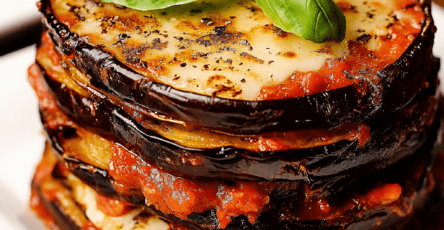Millefeuille italien d’aubergines gratinées servi dans un plat, avec couches d’aubergines dorées, sauce tomate, mozzarella fondue, parmesan et basilic frais.