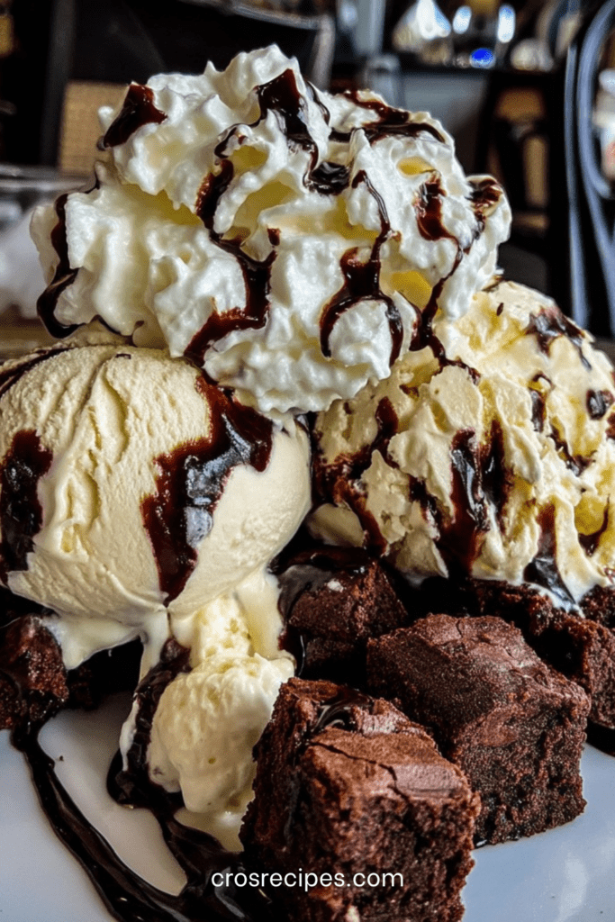 Brownie glacé servi en coupe avec morceaux de brownie fondant, boules de glace vanille, sauce chocolat tiède, chantilly et copeaux de chocolat.