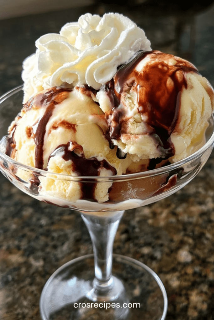 Coupe glacée vanille chocolat servie dans un verre à dessert, avec boules de glace vanille, sauce chocolat tiède, chantilly, copeaux de chocolat et amandes effilées.